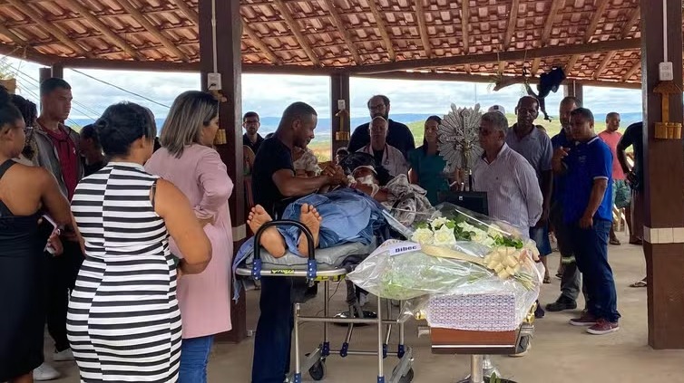 Deitada em maca, sobrevivente acompanha velório de filha em acidente com 24 mortos na Bahia